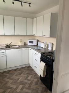 cocina con armarios blancos y estufa negra en SUNNY PRESTATYN APARTMENT, en Prestatyn