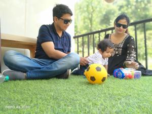 a man and woman and a child sitting on the grass with a soccer ball at Oak Retreat Huts in Shimla
