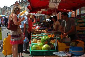 a woman standing in front of a market with fruits and vegetables at Onlycamp Camping le Champ d'été in Reyssouze