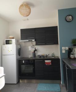 a kitchen with black cabinets and a white refrigerator at Aux portes de Nantes, 2 pièces moderne et confortable in Carquefou +2 photos