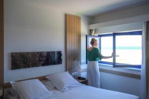 a woman looking out of a window in a hotel room at Thalazur Ouistreham - Hôtel & Spa in Ouistreham