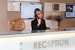 a woman talking on a cell phone behind a reception desk at Thalazur Ouistreham - Hôtel & Spa in Ouistreham
