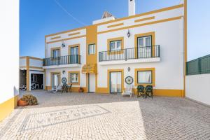 a large white and yellow building with chairs and tables at Apartamentos Pátio Victória by Umbral in Vila Nova de Milfontes