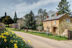 una vieja casa de ladrillo en un camino con flores en Church End Cottage, en Swerford