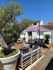 una terraza de madera con un árbol, sillas y una sombrilla en Maison Face au Soleil, en Le Bois-Plage-en-Ré