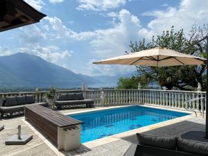 a swimming pool with an umbrella and chairs and a table at Romantic holiday home with a fantastic view of Lake Maggiore and the pool in Gordola