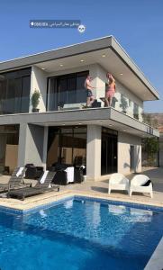 two people standing on the balcony of a house with a swimming pool at Follow Sea Villa in Sowayma