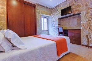 1 dormitorio con 1 cama y TV en una pared de piedra en Alojamento Central en Chaves