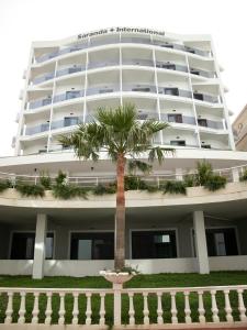 a large white building with a palm tree in front of it at Hotel Saranda International in Sarandë