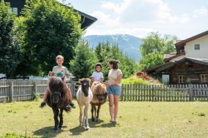 zwei Frauen und zwei Kinder reiten Ponys auf einem Feld in der Unterkunft Wawies Apartments in Flachau
