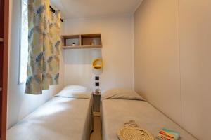 Dos camas en una habitación pequeña con ventana. en Le Cycas, mobil-home neuf avec sa vue dégagée sur les vignes et la mer, en Hyères