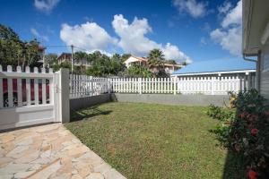 a white fence in front of a yard with grass at Villa Kaju : grande piscine et proche plage in Sainte-Luce