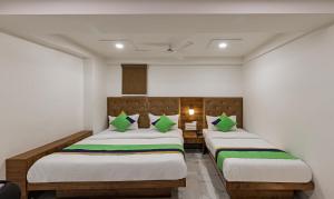 2 camas en una habitación con paredes blancas y almohadas verdes en Treebo Trend Prince Plaza en Ahmedabad