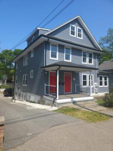 a gray house with red doors on a street at Modern Red Door Haven +5mins to Boston in Milton