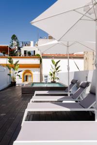 un patio con sillas blancas y una sombrilla en Lujoso apartamento con piscina compartida 2 en Sevilla