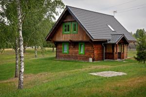 a small wooden house with green windows in a field at Domy Nad Drawskim in Siemczyno