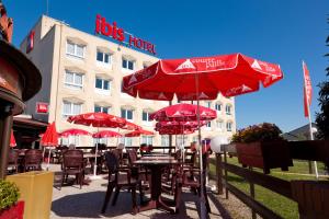 a tables with red umbrellas in front of a hotel at ibis Saint Dizier in Saint-Dizier