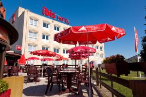 mesas con sombrillas rojas frente a un hotel en ibis Saint Dizier, en Saint-Dizier