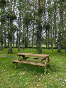um banco de madeira sentado na relva perto de árvores em La Maison des Amis en Normandie em Pontfarcy