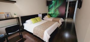 two beds in a hotel room with a green painting on the wall at Hotel Austral Suites in Cali