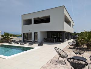 a large white house with chairs and a swimming pool at Villa SunSet in Privlaka
