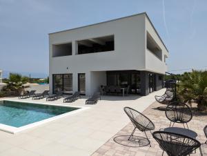a large white house with chairs and a swimming pool at Innova TravelVir - Villa SunSet in Privlaka