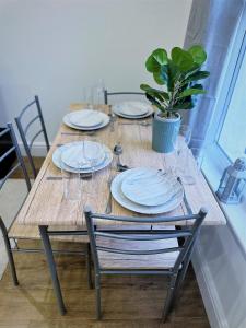 uma mesa de madeira com pratos e copos e um vaso de plantas em (ZONE 2) STYLISH 2 BED FLAT IN THE HEART OF LEWISHAM em Londres