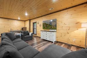 a living room with a couch and a tv in a wooden wall at New Cozy Mountain Cabin Hot Tub Near Downtown in Gatlinburg