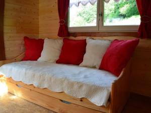 un lit en bois avec des oreillers rouges et blancs dessus dans l'établissement Roulotte cosy avec kitchenette, ruisseau apaisant et espace bien-être, nuit insolite à Ferdrupt - FR-1-589-444, à Ferdrupt
