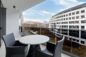 balcón con mesa y sillas blancas y ventana grande en Meriton Suites Canberra, en Canberra