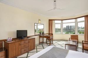 a room with a bed and a television and a desk at The Cama - A Sabarmati Riverfront Hotel in Ahmedabad