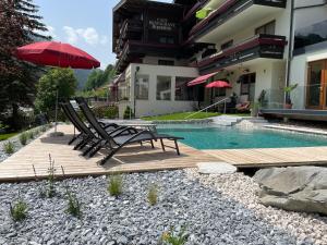 two chairs and an umbrella next to a swimming pool at Hotel Alpenblick in Saalbach-Hinterglemm