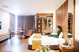 a woman sitting on a bed in a hotel room at IRIS Hotel Hải Phòng in Hai Phong