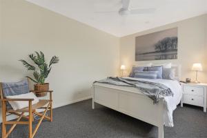 a white bedroom with a bed and a chair at Husky Sol in Huskisson