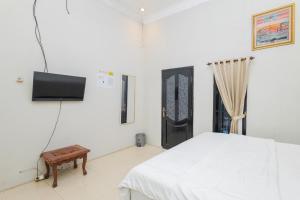 een witte slaapkamer met een bed en een televisie bij Boss Residence Serang Mitra RedDoorz in Kumprung