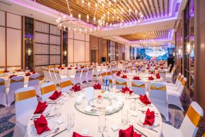 une grande salle de banquet avec des tables blanches et des serviettes rouges dans l'établissement Grand Hyams Hotel - Quy Nhon Beach, à Quy Nhơn