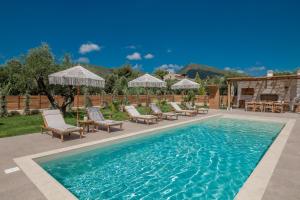 a pool with chairs and umbrellas on a patio at White Stone Villa Hesperia - Poolside Escape Close to Laganas Beach in Lithakia