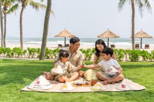 a family sitting on a picnic blanket on the beach at Danang Marriott Resort & Spa in Da Nang