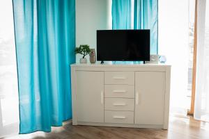 TV en una cómoda blanca con cortinas azules en Turkusowe tarasy apartament, en Czeladź
