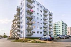 a tall white building with cars parked in a parking lot at Bm Apartamenty w Centrum Szczecin in Szczecin