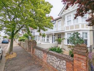 a white house with a stone wall and a tree at La Maison De La Mer, Worthing in Worthing