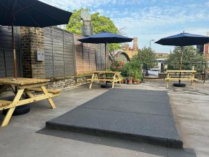 two picnic tables and umbrellas on a patio at Cricketers Hostel in London