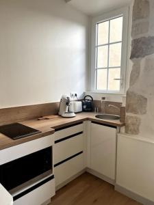 eine Küche mit weißen Schränken, einem Waschbecken und einem Fenster in der Unterkunft Le Petit Albert - Coeur de ville in La Rochelle