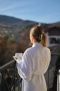 Eine Frau, die eine Tasse Kaffee auf einem Balkon hält. in der Unterkunft River Stone Hotel in Scheschory
