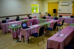 Grand Hotel Juba في جوبا: غرفة مع طاولات وكراسي وردية مع جهاز كمبيوتر محمول