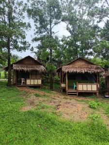 two huts with grass roofs in a field at Tony's Country Glamping with chalet with private wash room accommodation in El Nido