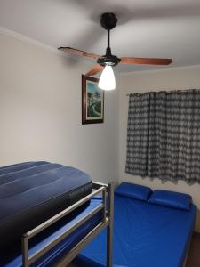 een slaapkamer met een plafondventilator en een blauw bed bij Na quadra da praia - Apto Completo Próximo a Estátua de Iemanjá - Vaga de Garagem e Wi-Fi in Praia Grande