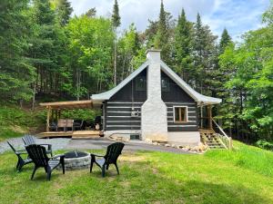 eine Hütte im Wald mit Stühlen im Hof in der Unterkunft Chalet du Sous-Bois By My Tremblant Location in Saint-Faustin