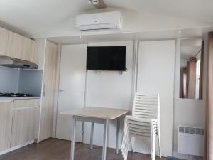 una pequeña cocina con mesa y 2 sillas blancas en Mobil home - Clim, TV - Camping '4 étoiles' - Narbonne Plage - 014, en Narbonne-Plage