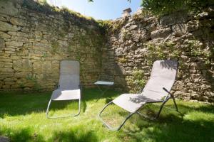 dos sillas sentadas en el césped junto a una pared de piedra en La Petite Maison du Périgord, en Tourtoirac
